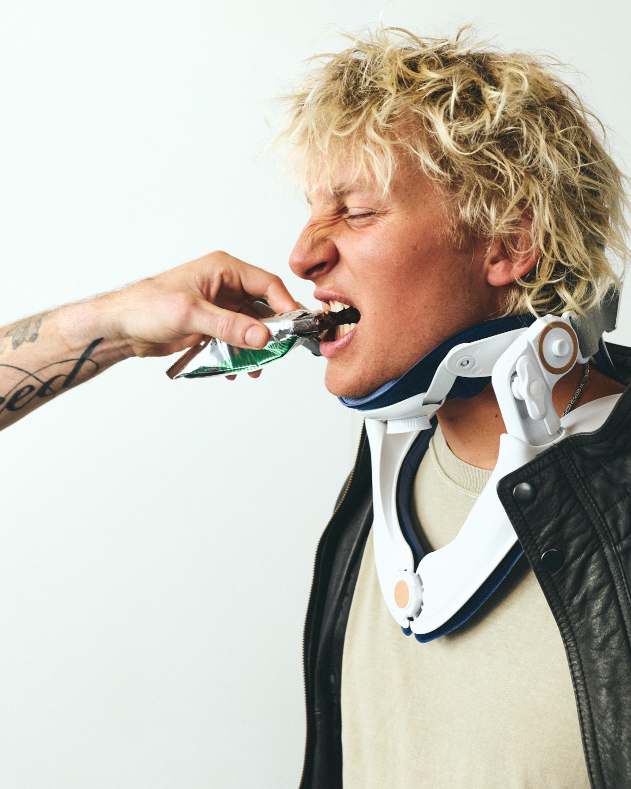 Ethan in a neck brace and leather jacket being fed an Unhinged bar