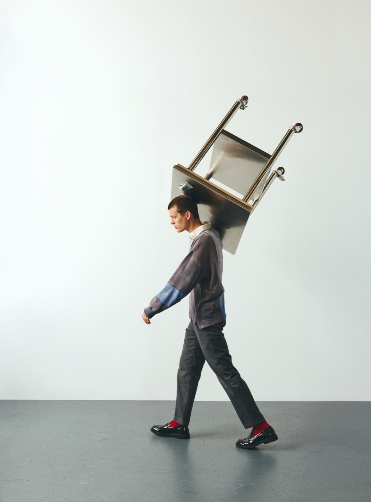 Bruce mid-stride with a steel work table balanced on his shoulder in the grey studio