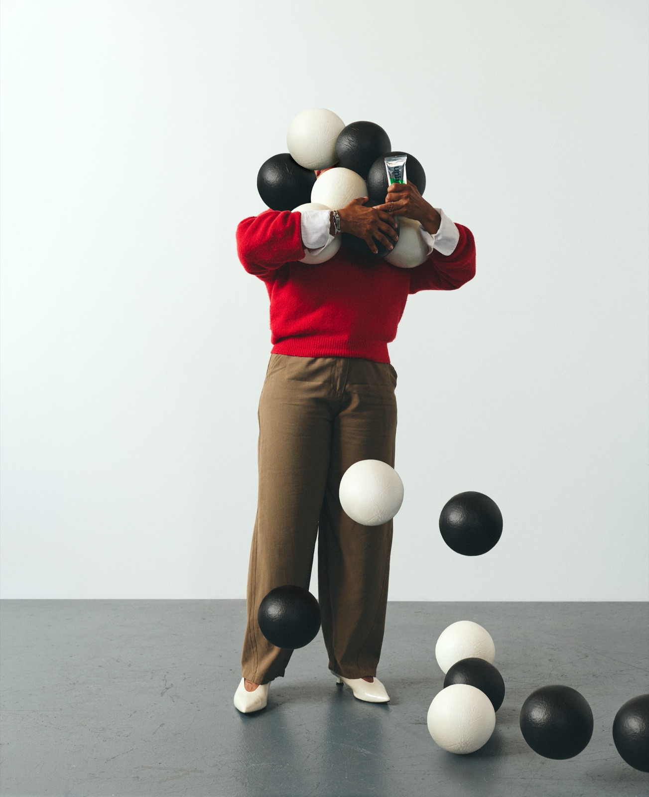 Diane in a red sweater mid-juggle, black and white balls dropping all around her on the grey studio floor