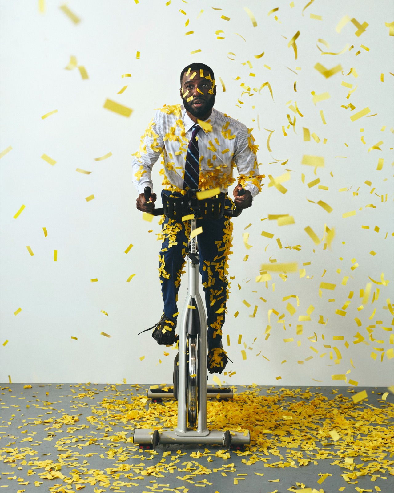 Marcus in office wear riding a spin bike through a storm of gold confetti